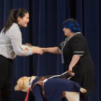 GSA President shaking hands with a professor receiving an award. The professor's service dog is onstage